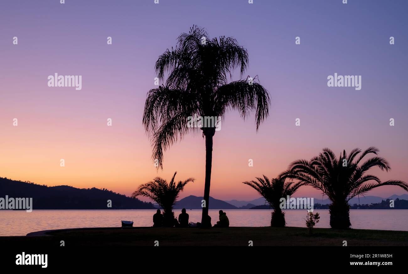 Silhouetten von Menschen am Strand bei Sonnenuntergang. Freunde treffen sich am Meer, Nachthimmel, Idee für Hintergrund oder Tapete Stockfoto