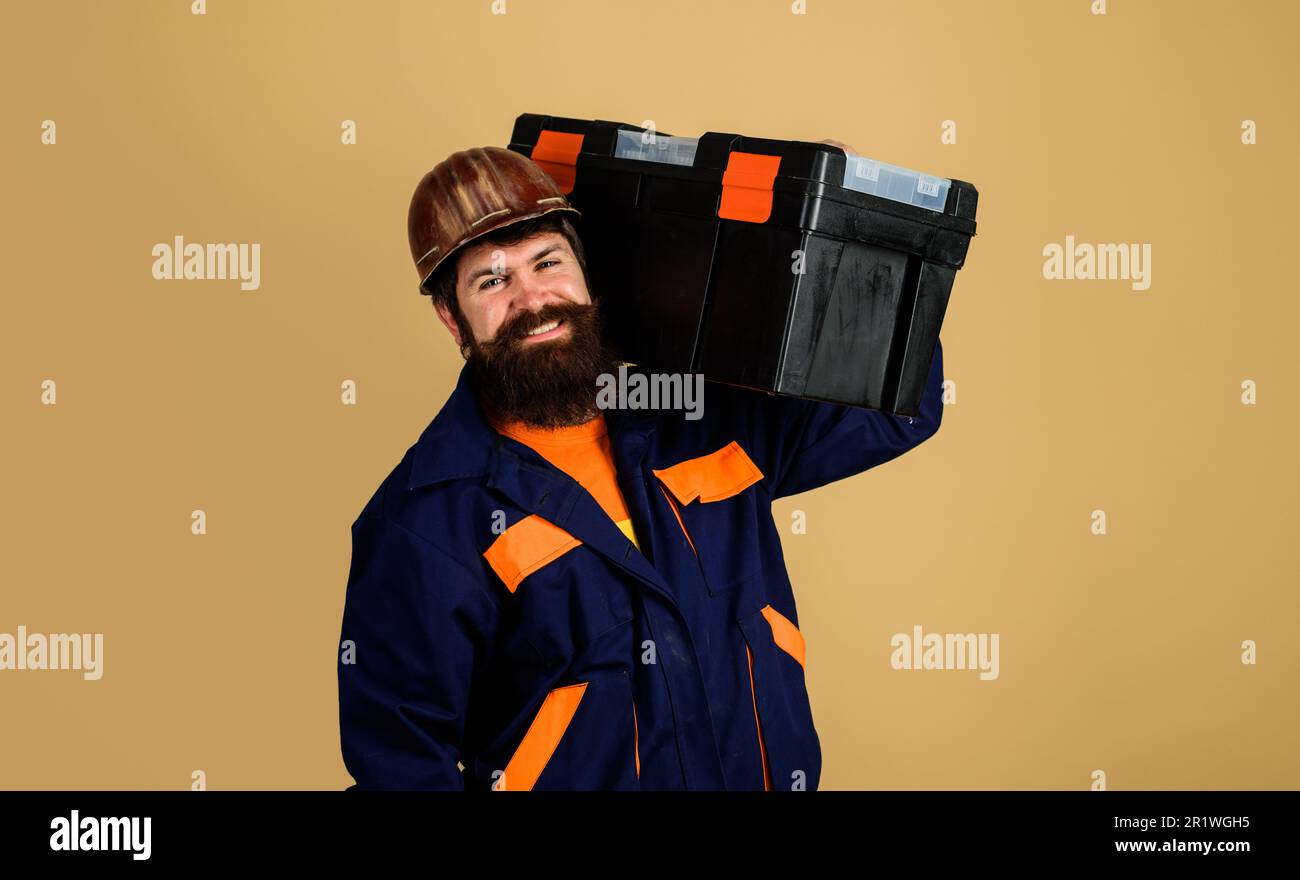 Heim reparieren. Mechaniker im Schutzhelm mit Werkzeugkasten. Handwerker, Handwerker mit Reparatursatz. Lächelnder bärtiger Mann in Bauernuniform mit Werkzeugkasten Stockfoto