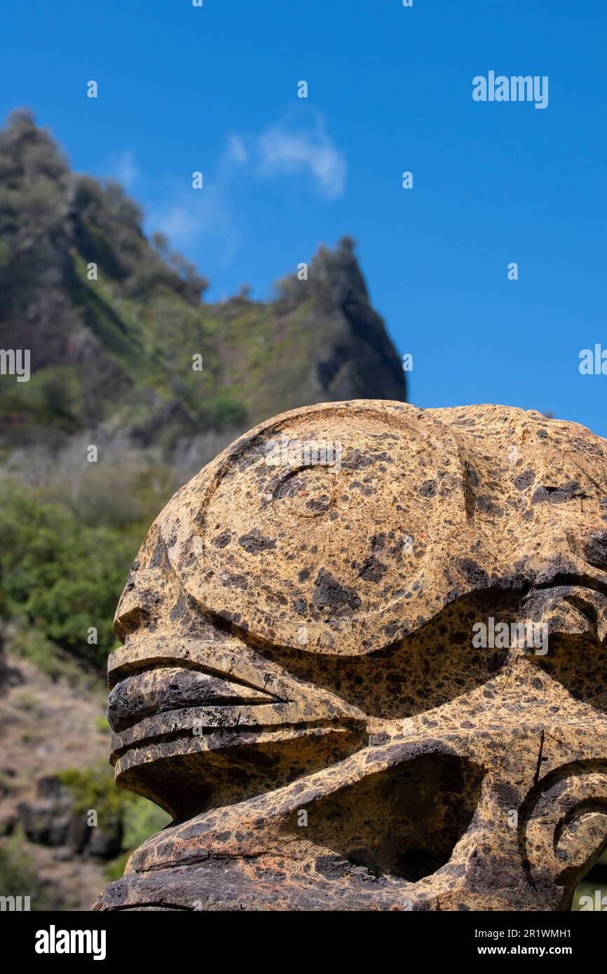 Französisch-Polynesien, Süd-Marquesas, Fatu Hiva, Dorf Omoa. Traditionelle Steinschnitzerei mit steilen vulkanischen Bergen in der Ferne. Stockfoto