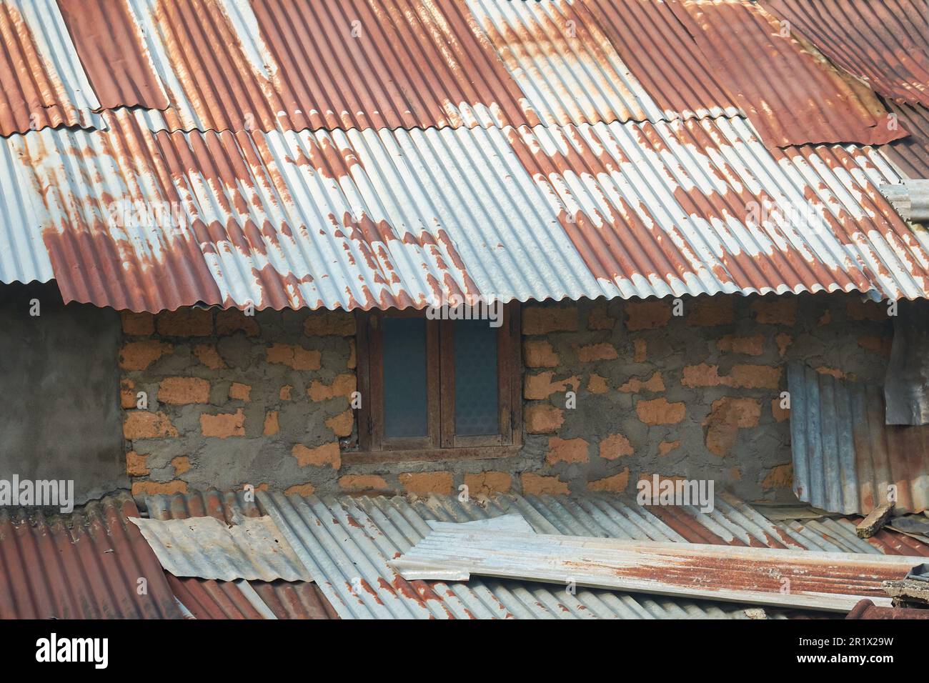 Nahaufnahme des alten beschädigten Dorfshütten, provisorisches Gebäude aus ungebrannten Ziegelmauern mit Zement und rostigen Wellblechen aus Metall Stockfoto