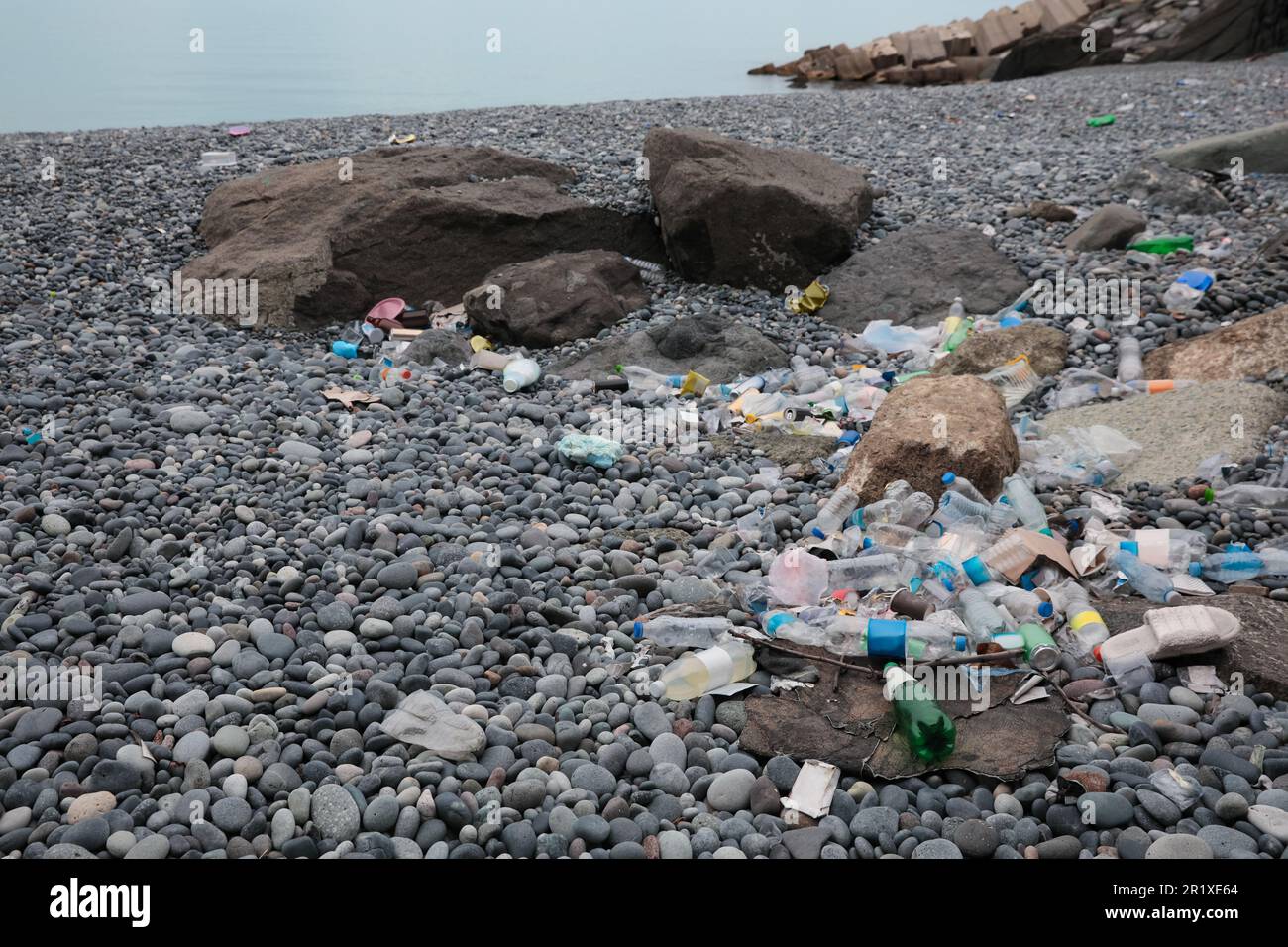 Müll verstreut auf Kieselsteinen nahe dem Meer. Recycling-Problem Stockfoto