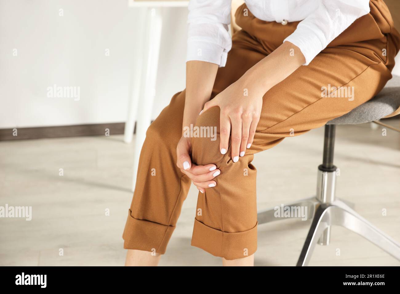 Eine Frau, die im Büro Kniescheiben reibt, Nahaufnahme. Platz für Text Stockfoto