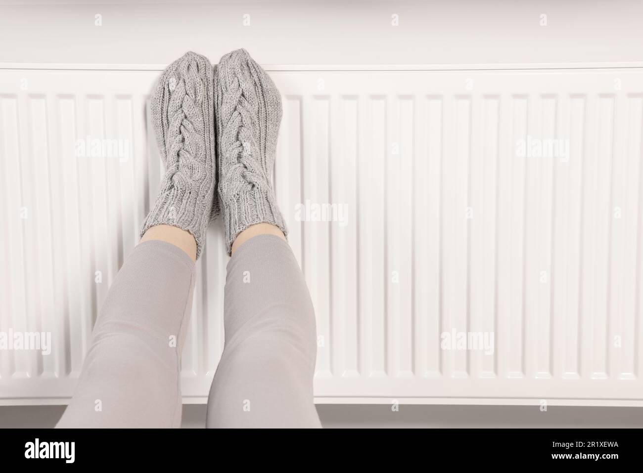 Frau wärmt Füße in der Nähe des Heizkörpers, Nahaufnahme. Platz für Text Stockfoto