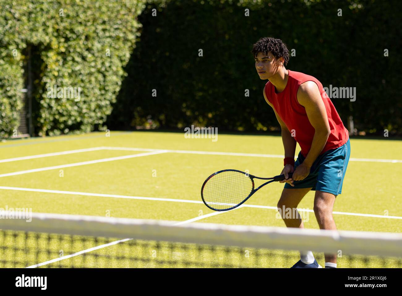 Ein birassistischer Mann mit Schläger, der darauf wartet, dass der Ball auf einem sonnigen Tennisplatz im Freien zurückkehrt, Kopierraum Stockfoto