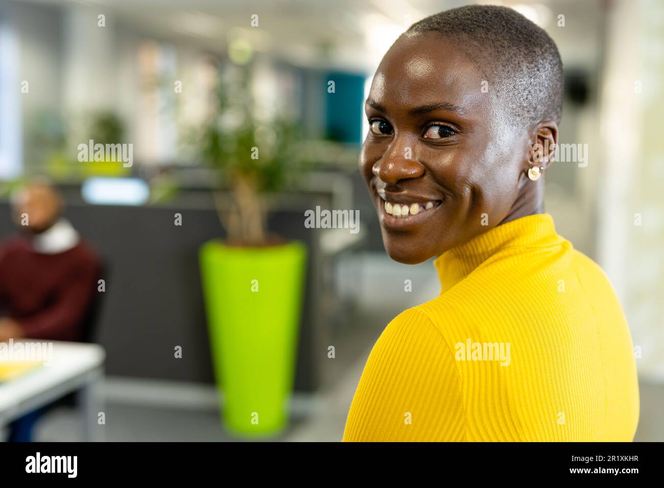 Porträt einer lächelnden afroamerikanischen Geschäftsfrau mit kurzen Haaren, die über die Schulter im Büro blickt Stockfoto