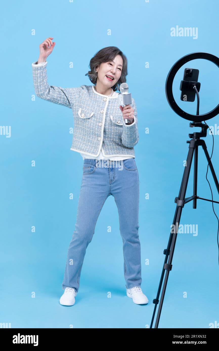 Sie singt eine aktive junge, leitende koreanische Asiatin mit Smartphone, mobilem Karaoke-Konzept Stockfoto