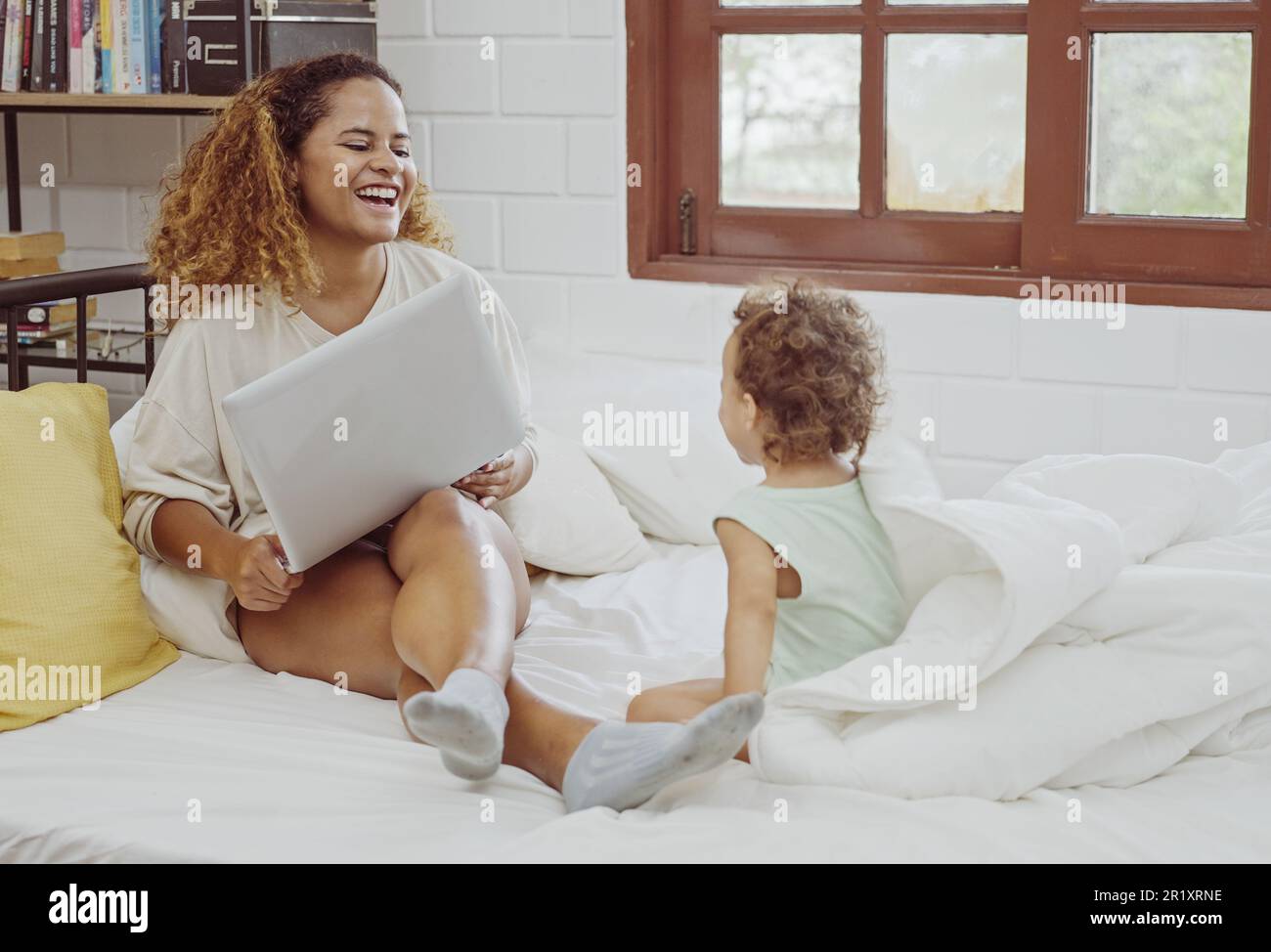 Junge Mutter, die ihren Laptop für die Arbeit in der Nähe ihrer Tochter im Bett benutzt. Stockfoto