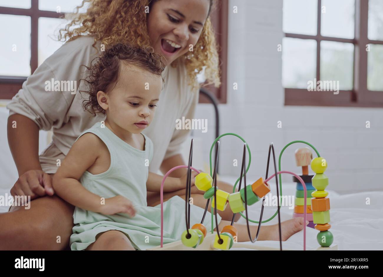 Glückliche Mutter und Tochter spielen mit einem Spielzeug, das zu Hause auf dem Bett farbenfrohe Holzblöcke entwickelt. Stockfoto