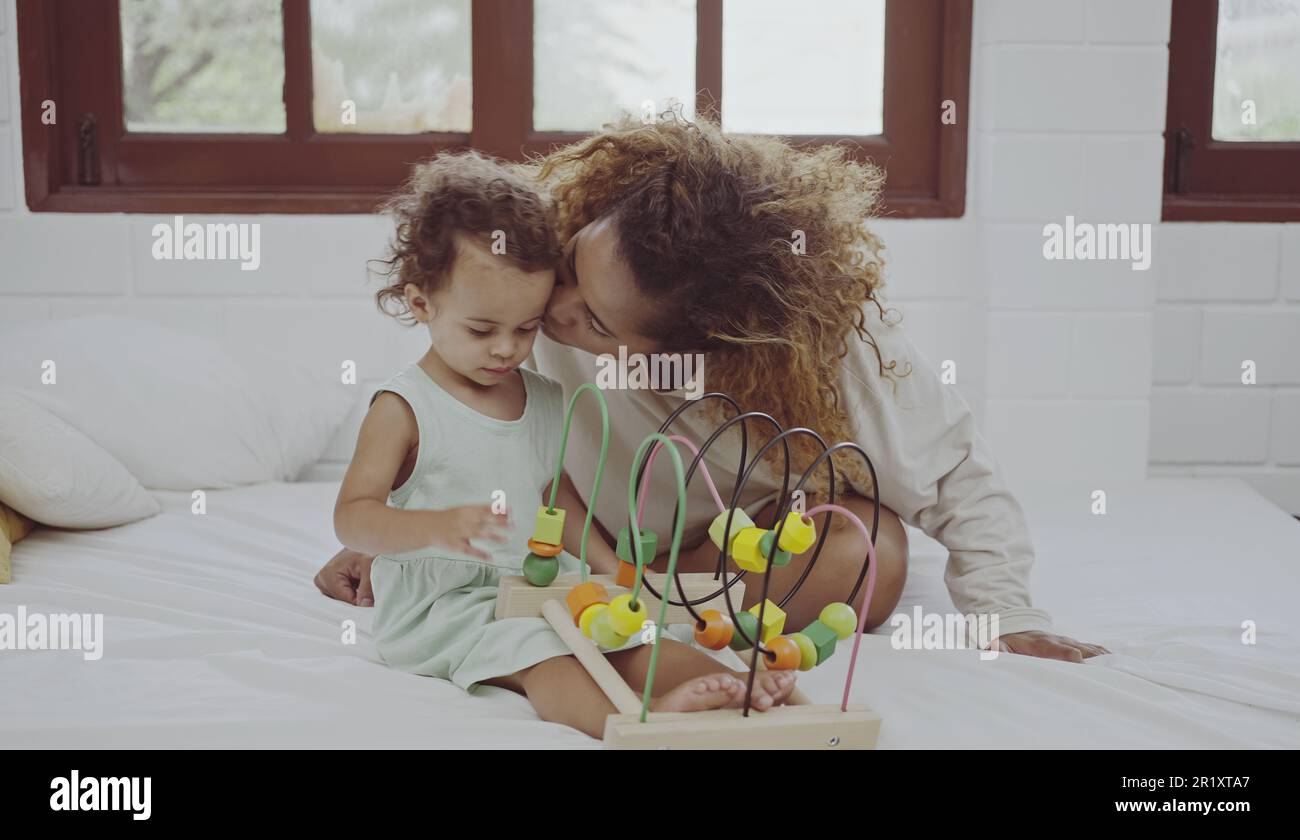 Glückliche Mutter und Tochter spielen mit einem Spielzeug, das zu Hause auf dem Bett farbenfrohe Holzblöcke entwickelt. Stockfoto