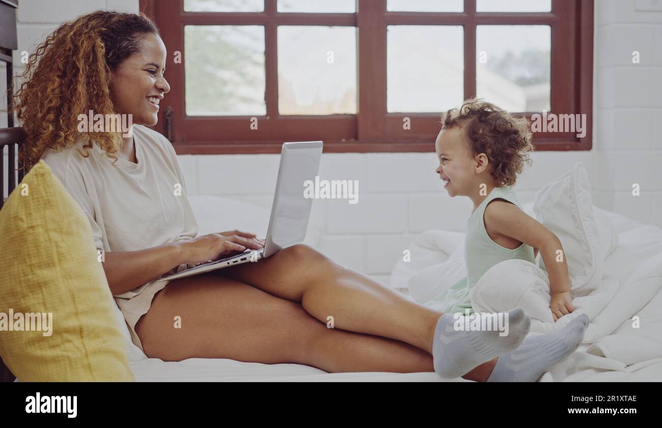 Junge Mutter, die ihren Laptop für die Arbeit in der Nähe ihrer Tochter im Bett benutzt. Stockfoto