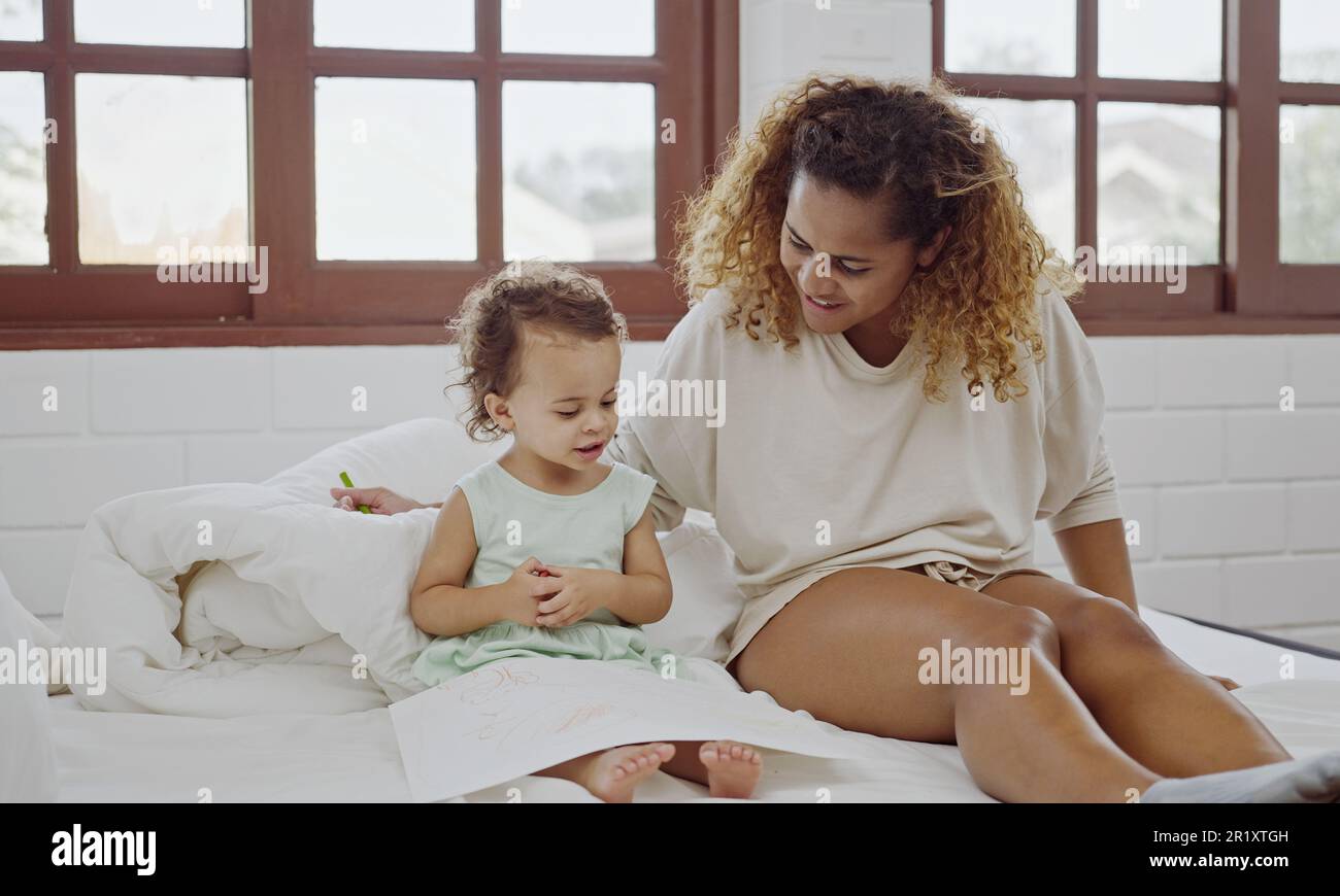 Junge Mutter, die auf dem Bett sitzt und mit ihrer kleinen Tochter malt. Stockfoto