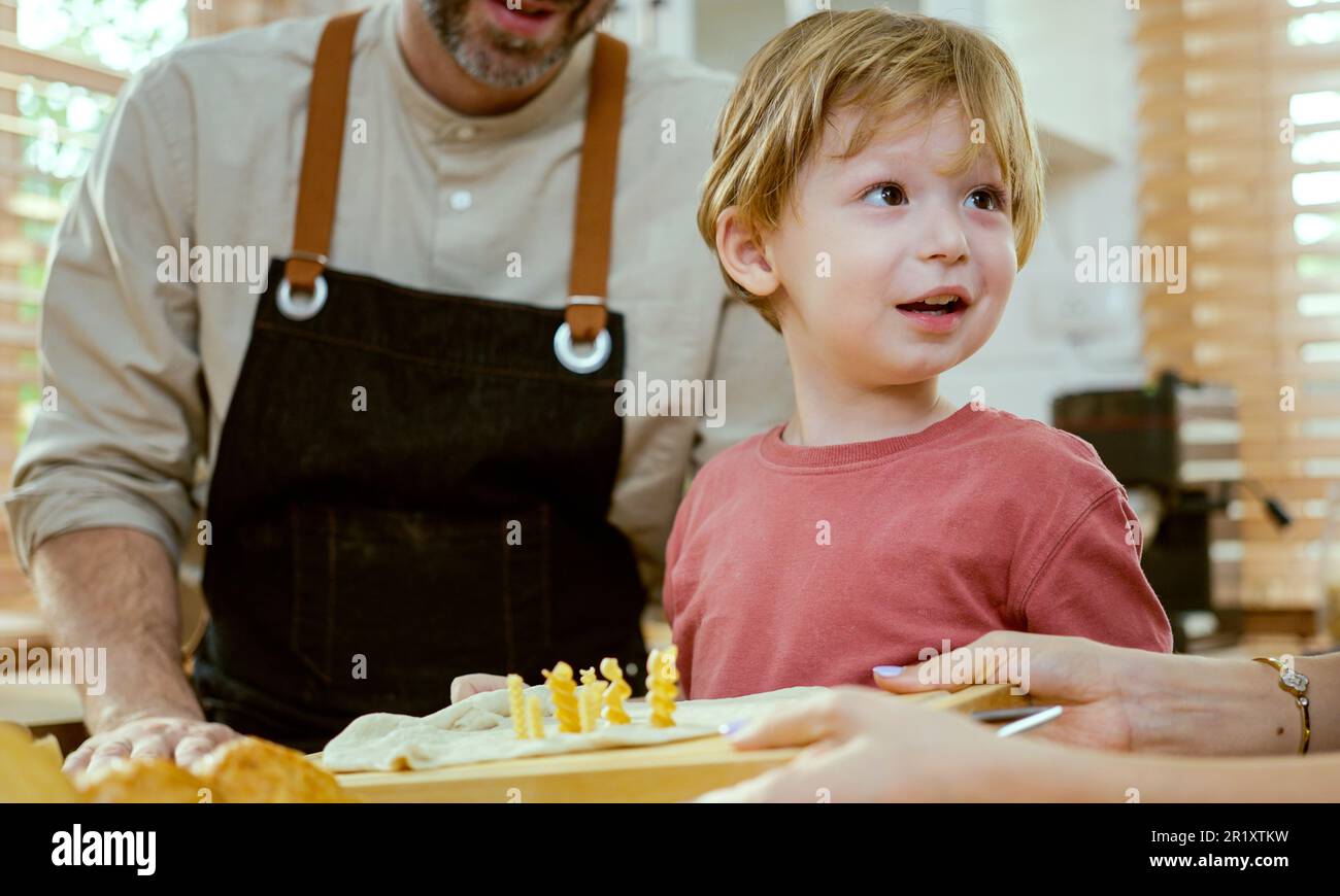Glückliche junge Familie, die gerne Kuchenteig oder Gebäck in der modernen Küche zubereitete, sehr glückliche Eltern, die dem kleinen Sohn beibrachten, wie man zu Hause Bäckerei kocht Stockfoto