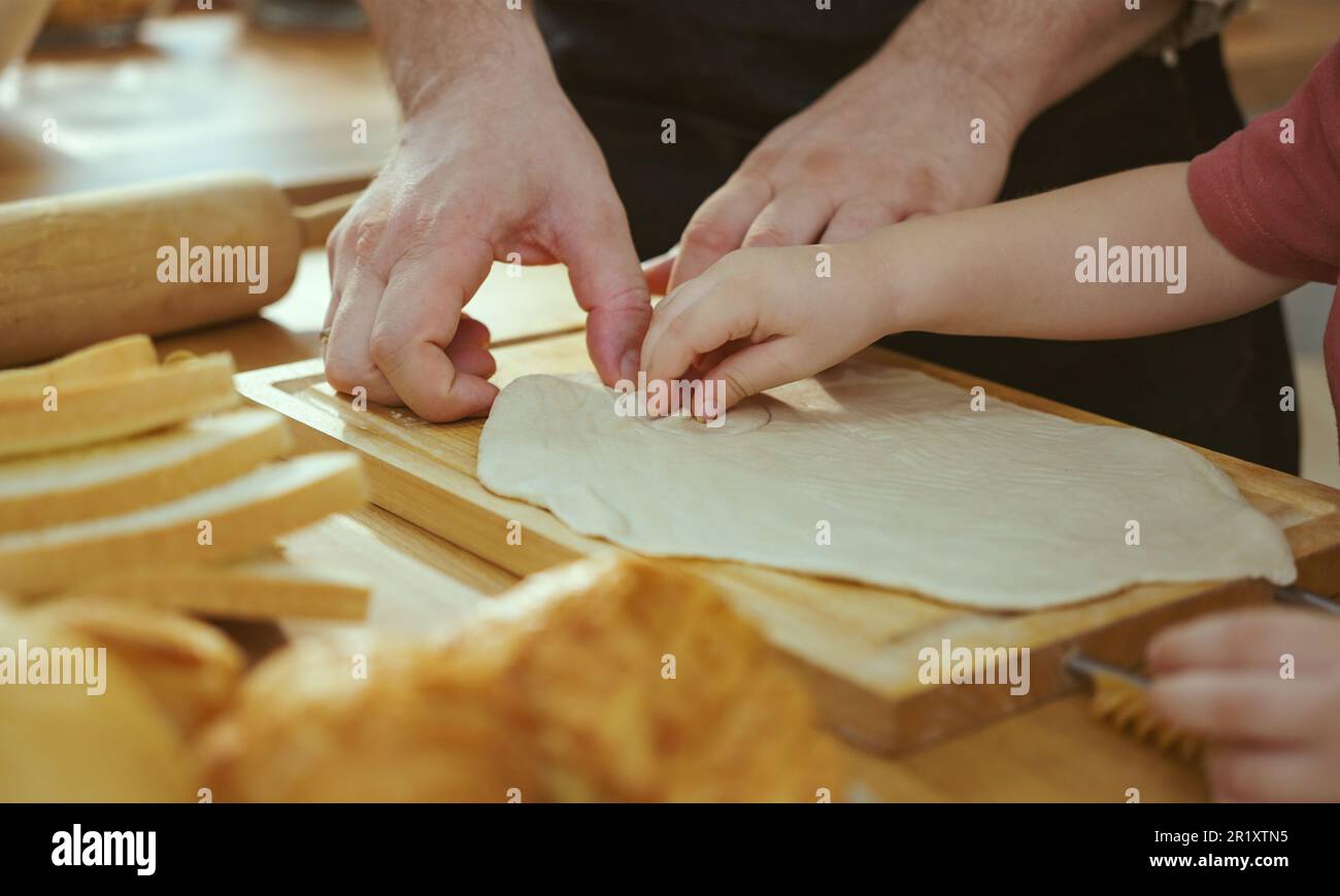 Glückliche junge Familie, die gerne Kuchenteig oder Gebäck in der modernen Küche zubereitete, sehr glückliche Eltern, die dem kleinen Sohn beibrachten, wie man zu Hause Bäckerei kocht Stockfoto