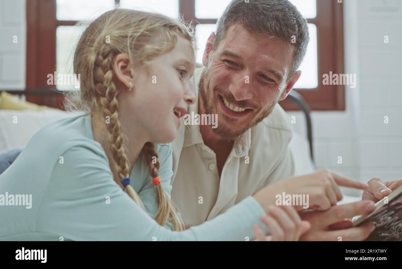 Vater und Tochter lesen ein Geschichtenbuch auf dem Bett. Stockfoto