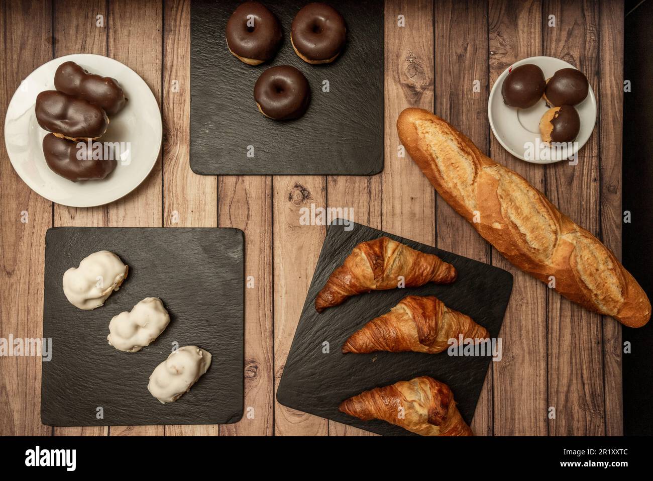 Ein Schieferteller mit einfachen Schokoladenbonbons, Buttercroissants und einem Laib Brot Stockfoto