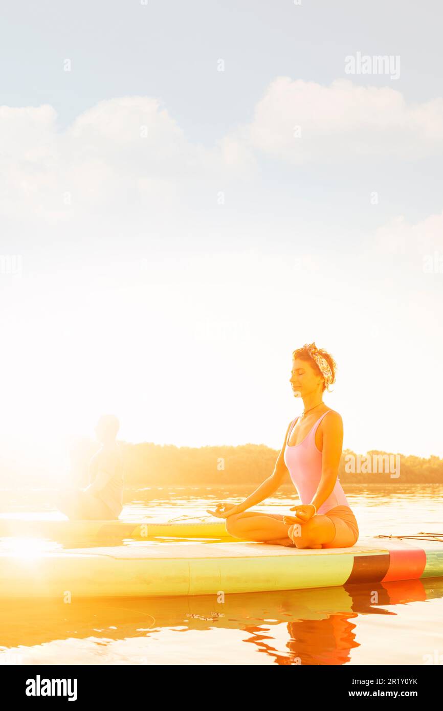 „Seelische Gesundheit fördern mit SUP Yoga: Junge Frau und Mann üben zusammen Stockfoto