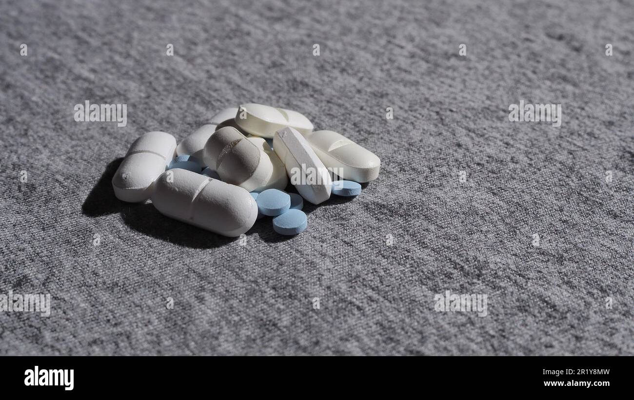 Detailaufnahme eines Stapels verschiedener medizinischer Pillen auf grauem Hintergrund mit Kopierraum und selektivem Fokus Stockfoto