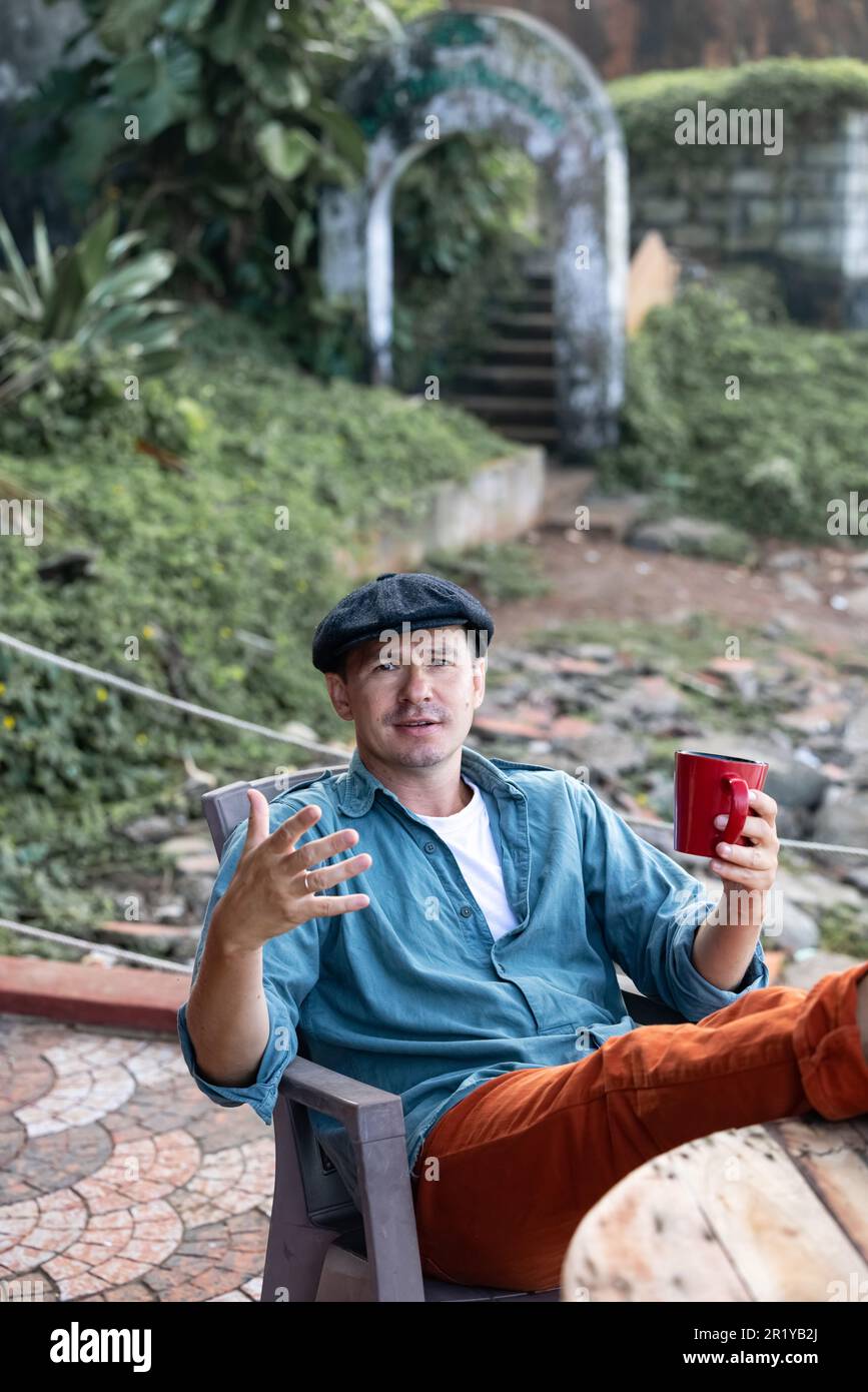 Der Mann, der einen Hut trägt, spricht, während er Kaffee aus einem roten Becher trinkt Stockfoto