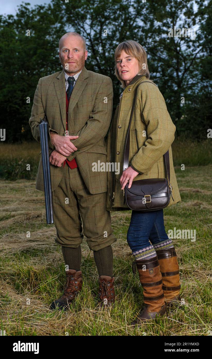 Eine englische Dame und ein Gentleman standen in der Dämmerung in Schießanzügen mit einer Schrotflinte Stockfoto