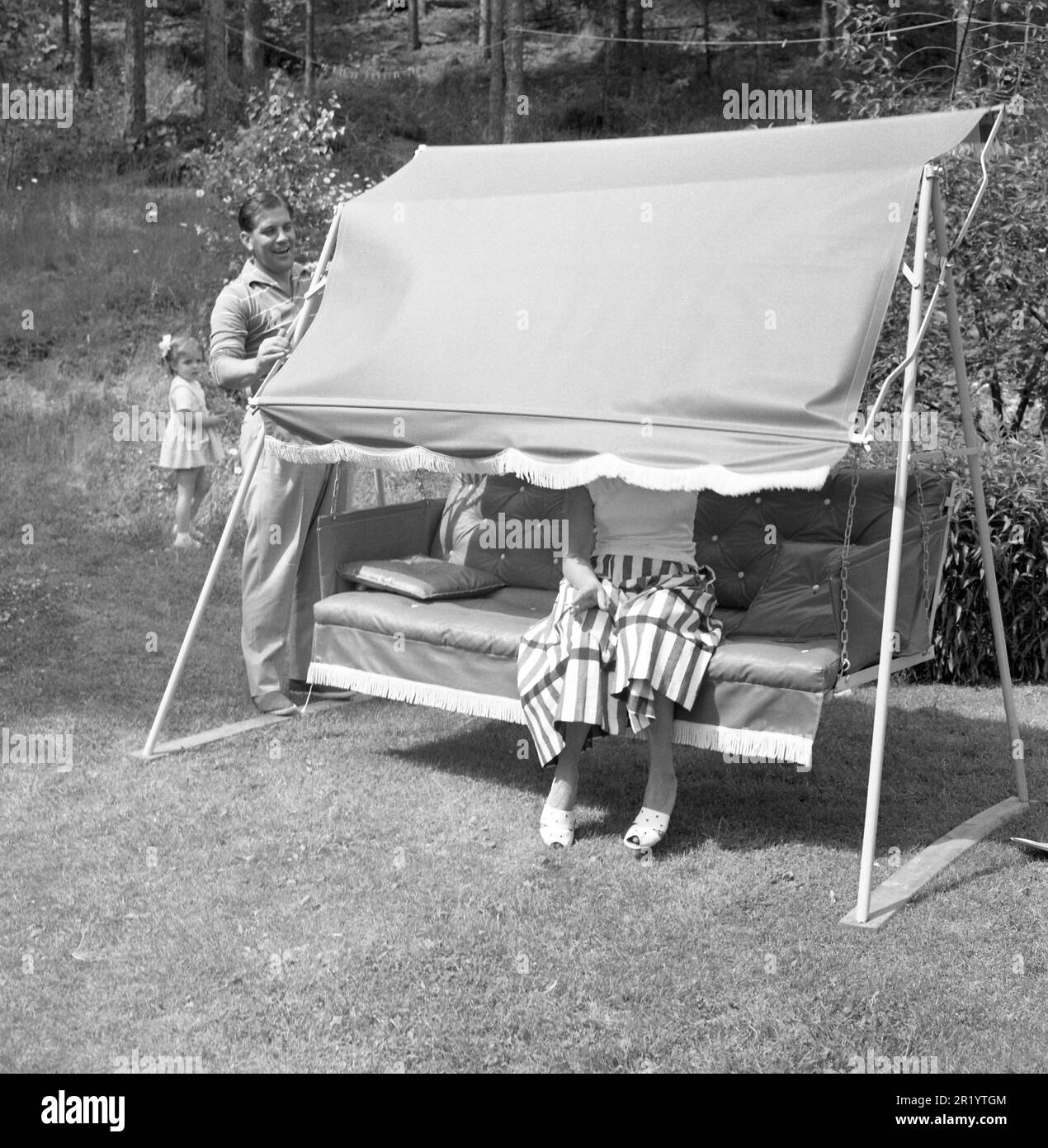 Sommer in den 1950er Jahren. Eine Frau sitzt in einer Hängematte, aber ihr Mann spielt mit ihr und kippt die obere Abdeckung so, dass sie nicht sehen oder gesehen werden kann. Er ist der berühmte schwedische Fußballspieler Gunnar Nordahl, 1921-1995, legendäres Mitglied des italienischen AC Mailand im Trio GRE-No-Li. Schweden 1957. Conard Ref. 3498 Stockfoto