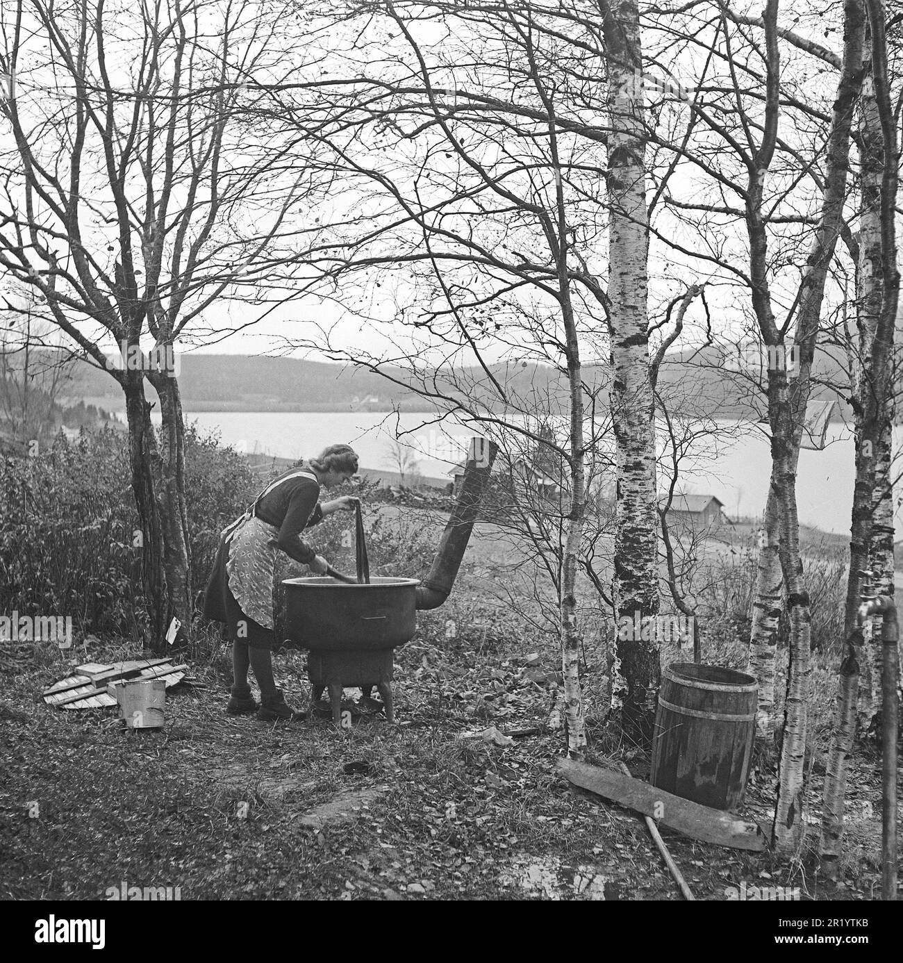 Der Fotograf ist in Ångermanland, genauer gesagt im Dorf Näs außerhalb von Örnsköldsvik. Hier folgt er der Familie Karlsten für ein paar Tage und erstellt ein nostalgisches Zeitdokument für zukünftige Generationen. Frau Anna Karlsten, die sowohl die Hausfrau als auch die Frau und Managerin des Bauern ist. Sie ist Eigentümerin des Familienunternehmens Kornsjö Trävaru ab. Hier ist die Tochter Ebba Karlsten, die im Freien mit dem Färben von Wolle arbeitet, ein Wissen, das bereits 1942 aufgrund der Industrialisierung als fast vergessen galt. Ein einfacher, aber praktischer holzbrennender Wasserkocher erleichtert die Arbeit. In Europa die Stockfoto