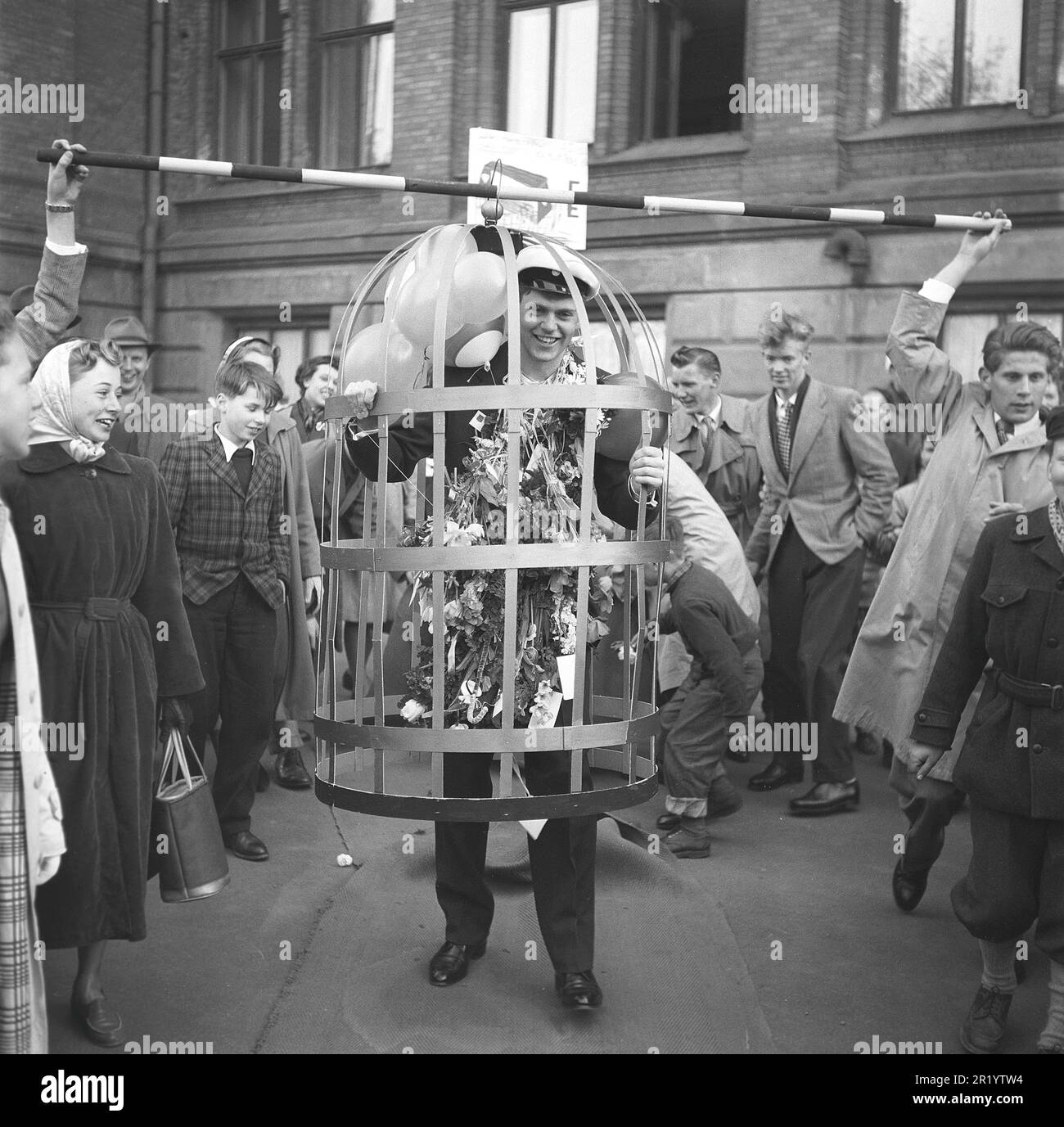 In den 1950er Jahren. Der Abschlusstag, an dem die Prüfungen beendet und die Schule verlassen wird, ist in der Regel ein festlicher Tag mit Familie und Freunden, an dem die Leistungen der Schüler gefeiert werden, indem sie ihn mit Kostümen streicheln und ihm Geschenke und Blumen schenken. Dieser junge Mann wird in einen Käfig gesteckt und auf der Straße vorgeführt. Schweden 1953 Kristoffersson Ref BL79-1 Stockfoto