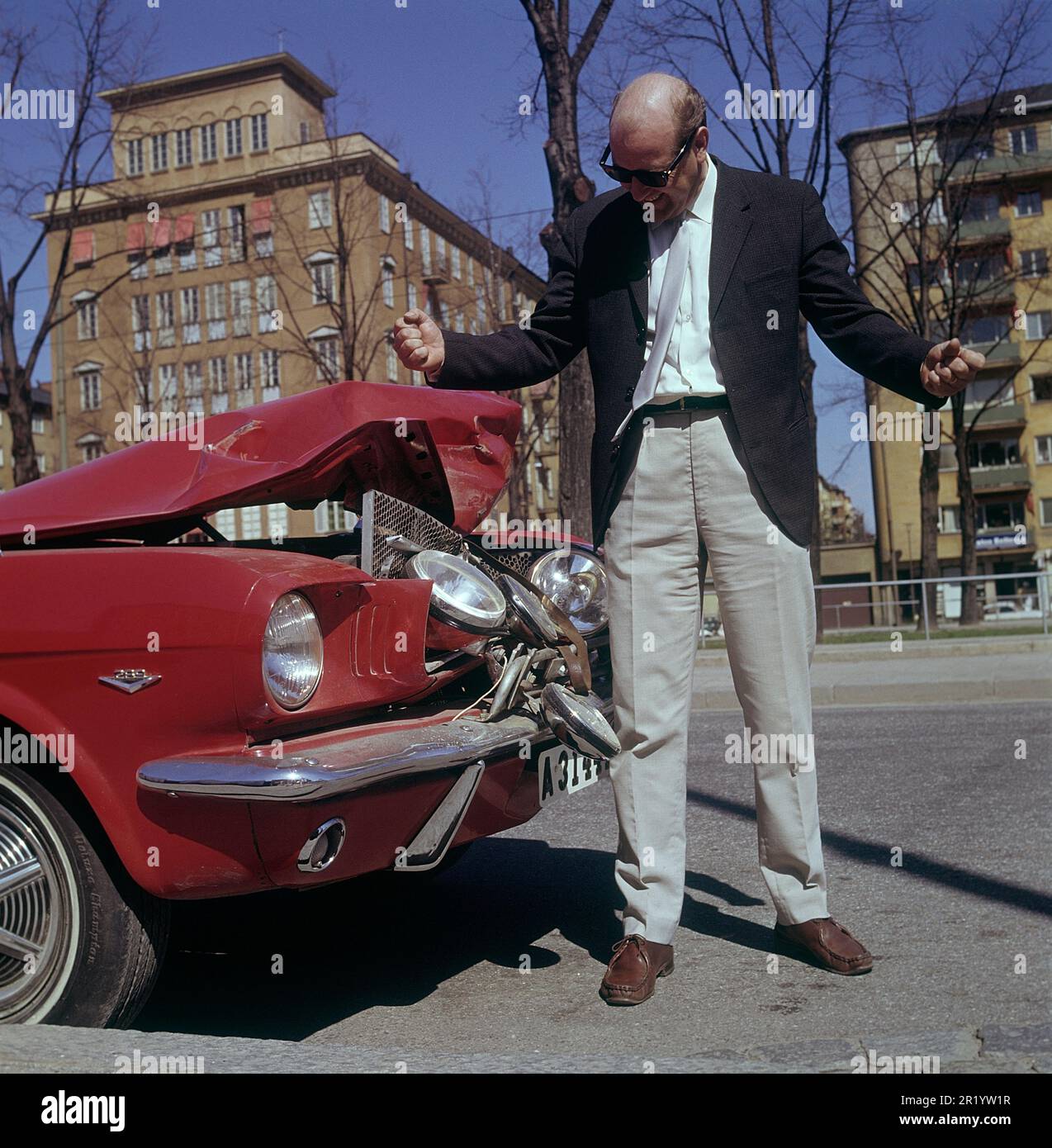 Fahren in der 1960er. Ein Mann steht vor seinem Auto, das bei einem Verkehrsunfall sichtbar beschädigt wurde. Ein Frontalaufprall oder jemand ist in sein Auto zurückgefahren. Er sieht frustriert aus. Schweden 1969 Kristoffersson Stockfoto