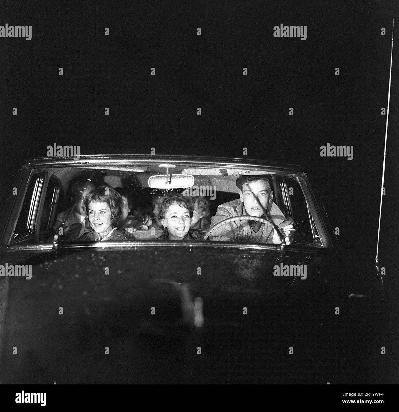 Fahren in der 1950er. Ein junger Mann auf dem Fahrersitz mit zwei jungen Frauen neben ihm auf dem Vordersitz. Er konzentriert sich darauf, in der dunklen Nacht zu fahren, und seine Augen sind auf der Straße, da es in einer regnerischen Nacht ist. Schweden 1959. ref. BV99-12 Stockfoto