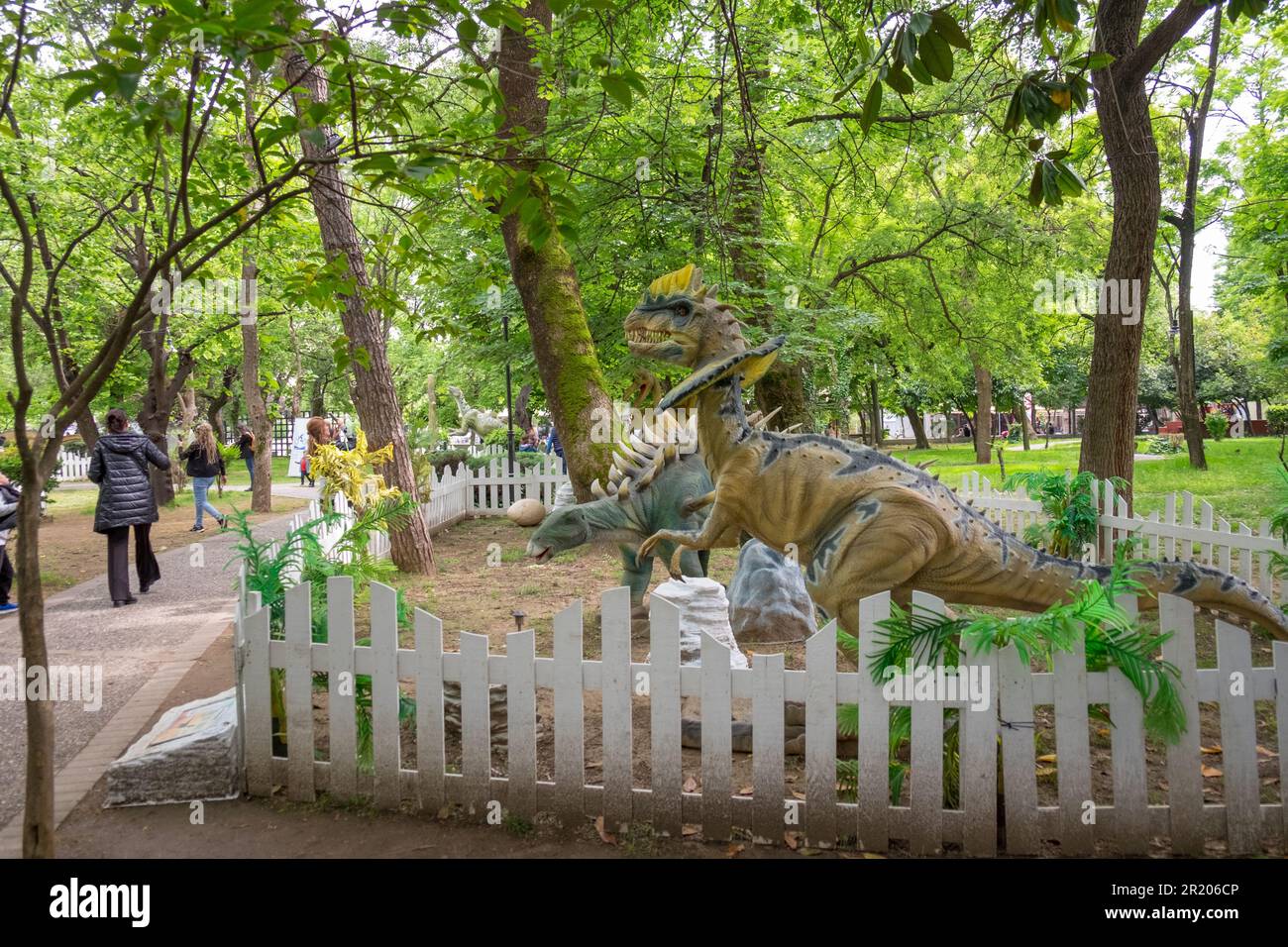 Erwachsene und Kinder starren die animatronischen oder roboterartigen Dinosaurier in einem Park an Stockfoto