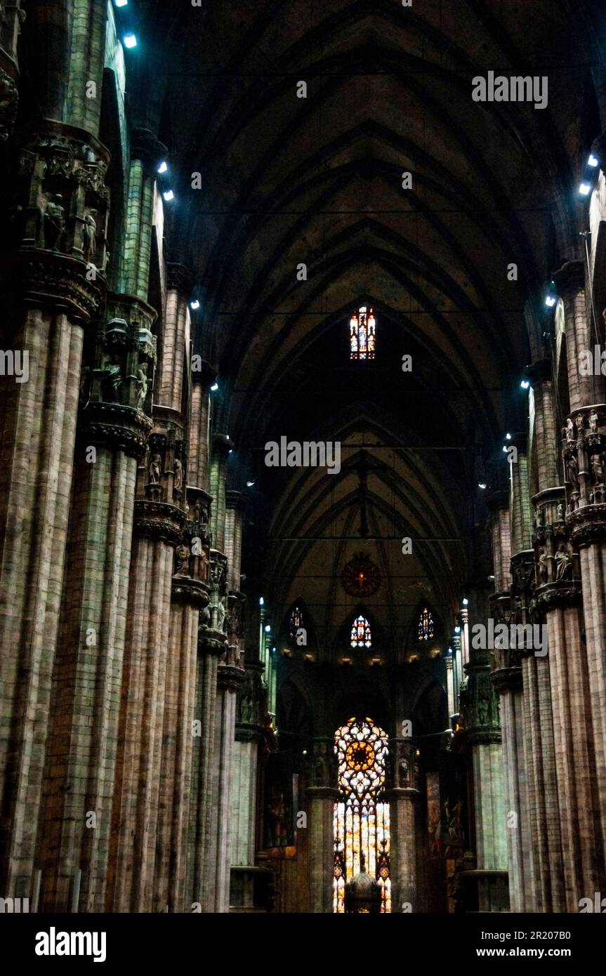 Riesige, gruppierte Säulen, geschnitzte Statuetten auf Kapitolen und das rote Licht in der Mailänder Kathedrale in Mailand, Italien. Stockfoto