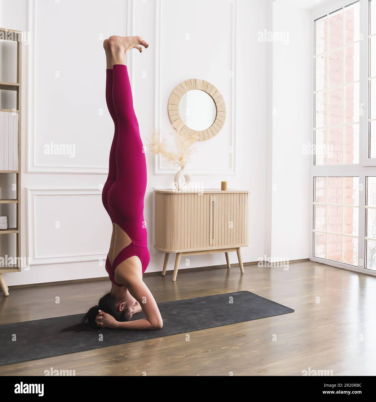 Eine junge Frau, die einen gesunden Lebensstil führt und Yoga praktiziert, führt das Shirshasana-Training durch, umgekehrtes Asana, Ellenbogenständer mit gestreckten Beinen, Stockfoto