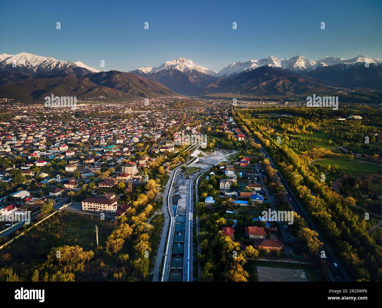 Draufsicht über den großen Fluss Almaty und die Häuser mit der Kulisse der Schneebirge im Hintergrund in der Stadt Almaty, Kasachstan Stockfoto