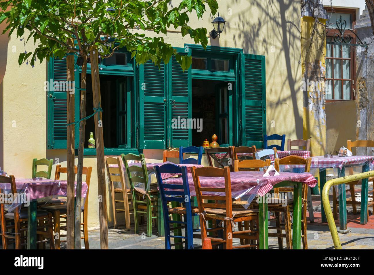 Rustikale mediterrane Taverne oder zwangloses Straßenrestaurant mit verschiedenen bemalten Holzstühlen an den Tischen vor den Fenstern einer traditionellen Hure Stockfoto