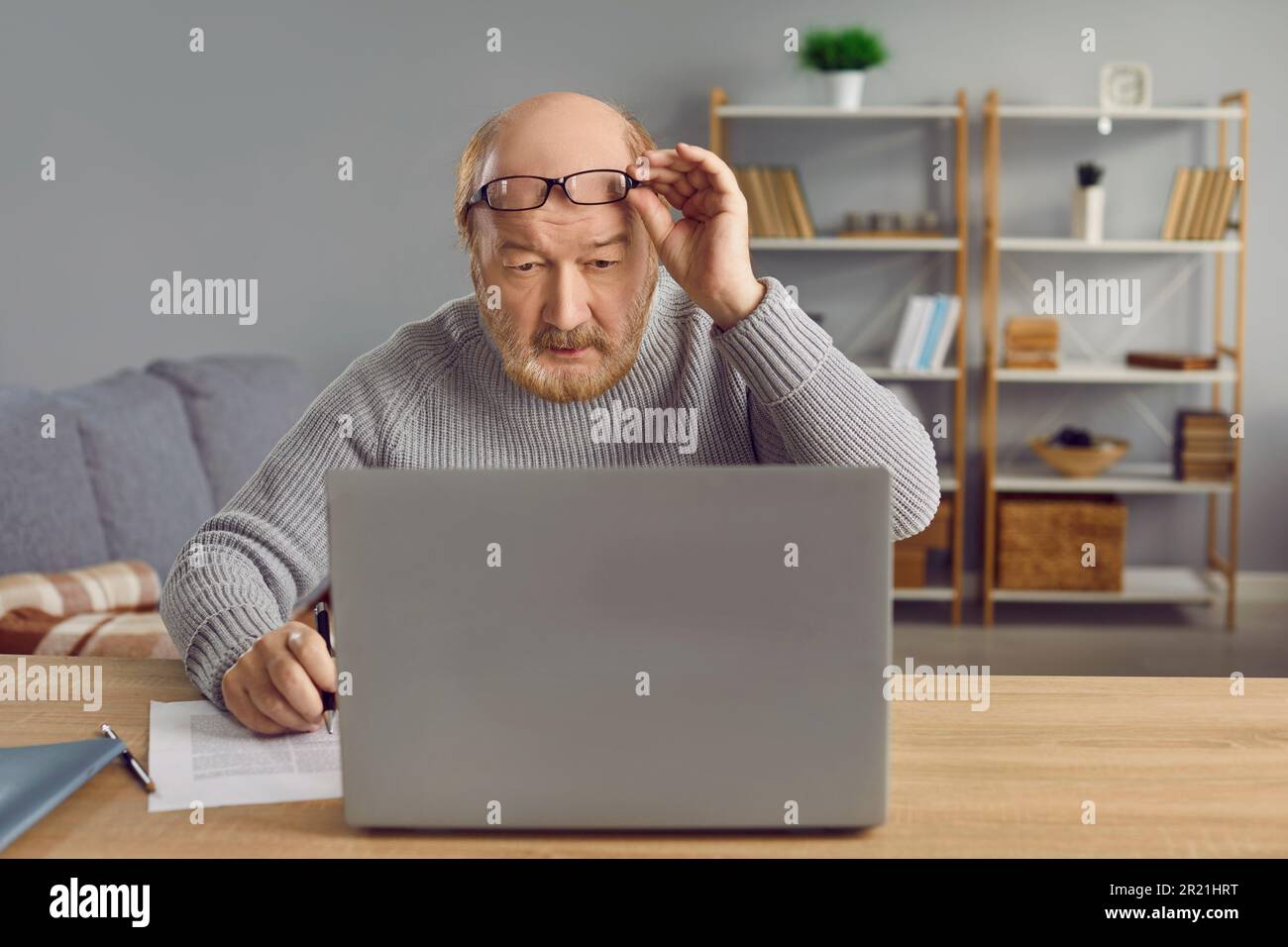 Porträt eines Seniorenmannes, der mit erhobener Brille auf einen Laptop-Bildschirm schaut Stockfoto
