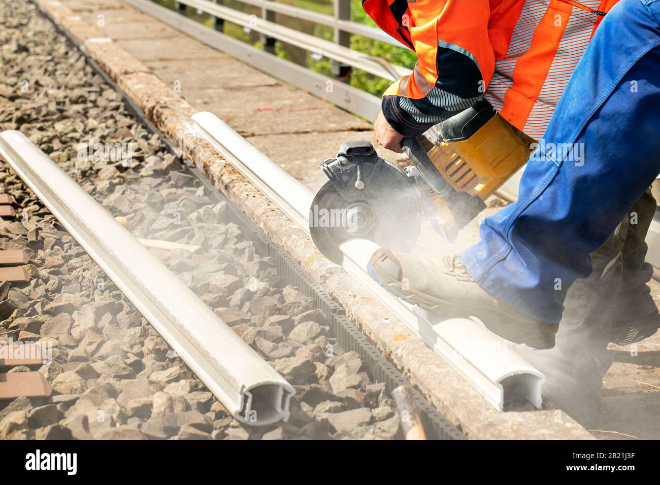 Ein Arbeiter in Arbeitskleidung und Warnweste schneidet mit einer Handkreissäge ein Stück Kunststoff-Kabelkanal ab. Ein Kollege in der Arbeit, Gerinnsel Stockfoto