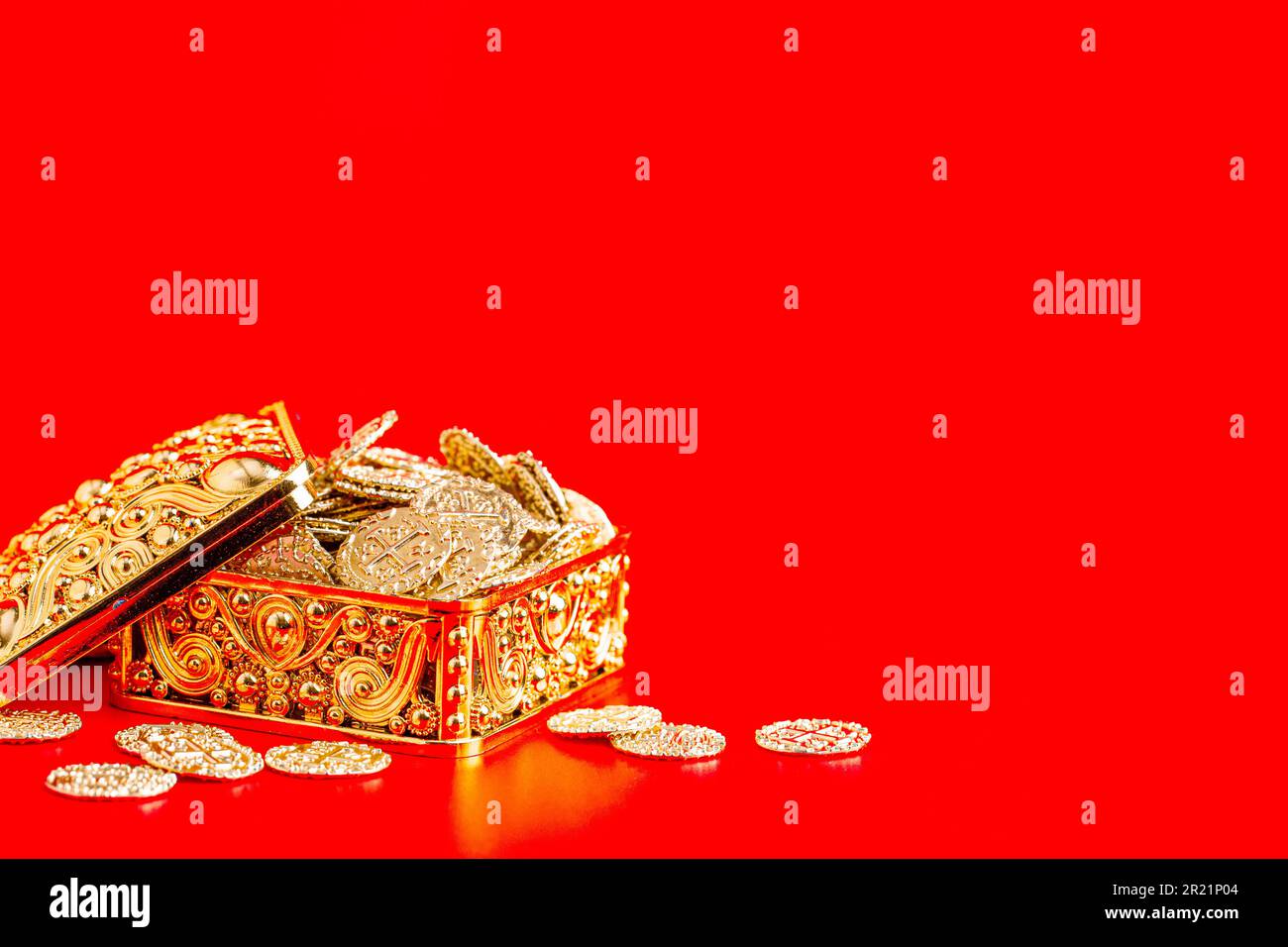 Goldene Kiste mit goldenen Münzen, isoliert auf rotem Hintergrund Stockfoto