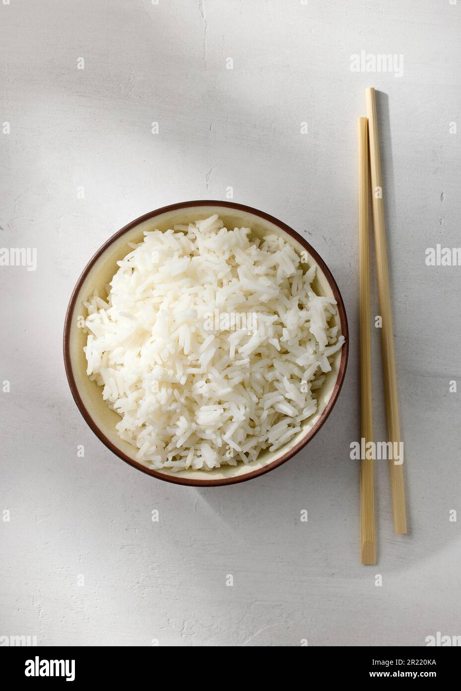 Schüssel mit gekochtem Reis und Essstäbchen auf weißem Küchentischhintergrund, Draufsicht Stockfoto