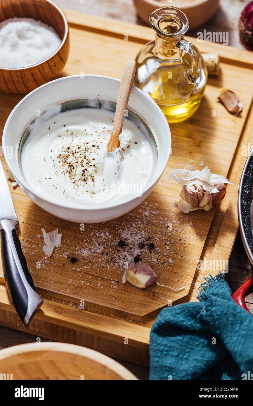Backpfanne gefüllt mit Roastkartoffeln oder gebackenen Pommes frites in einer chaotischen Arbeitsküche mit einer Schüssel Joghurt-Sauce, Olivenöl, Knoblauch und Gewürzen und Con Stockfoto