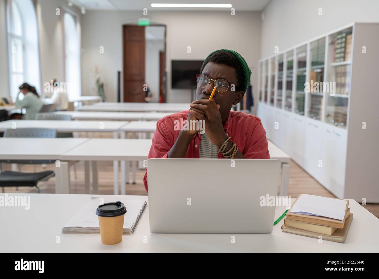 Rücksichtsvoller afroamerikanischer Nerd-Student, der mit einem Laptop in der Bibliothek lernt. Stockfoto
