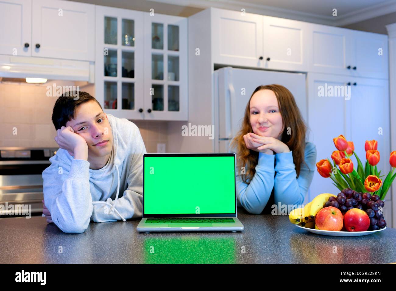 Junge Mädchen in der Küche in der Nähe eines Laptops mit grünem Bildschirm schauen Filme online Training Interessantes Internet soziale Netzwerke Essen Frühstück liefern jede Werbung auf grünem Bildschirm Chroma Key Stockfoto