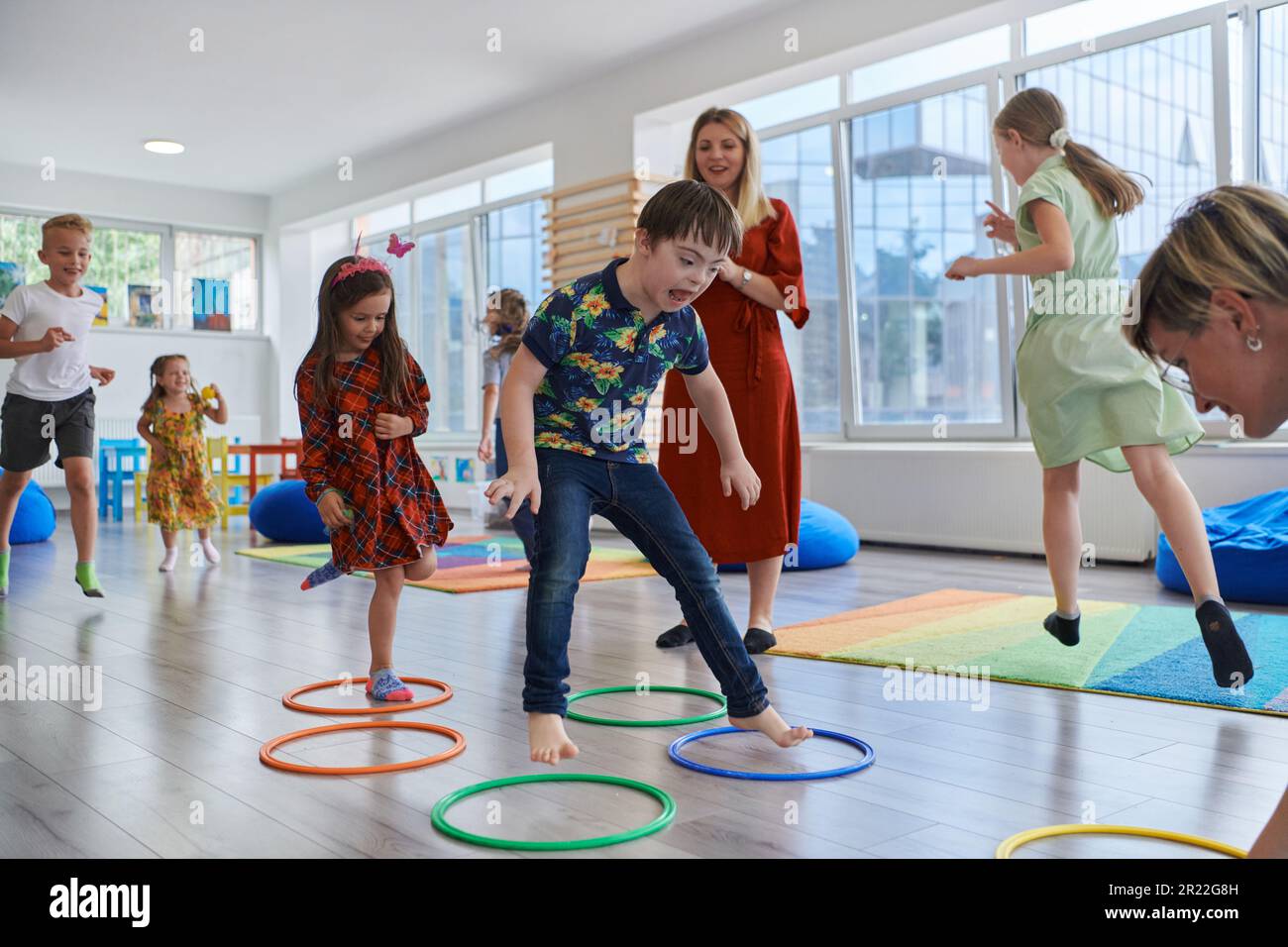Kinder Springen Kleine Kinder im Kindergarten mit Lehrerin auf dem Boden drinnen im ...