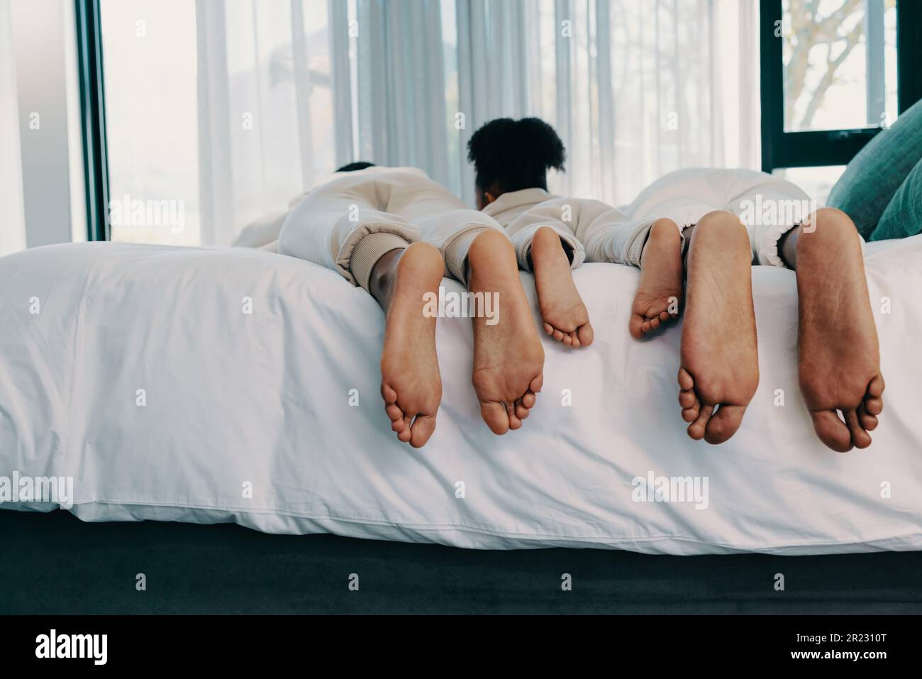 Familienwochenende: Zwei Eltern und ihre Tochter liegen mit ausgestreckten Füßen auf einem Bett. Eine dreiköpfige Familie knüpft an die Hure Stockfoto
