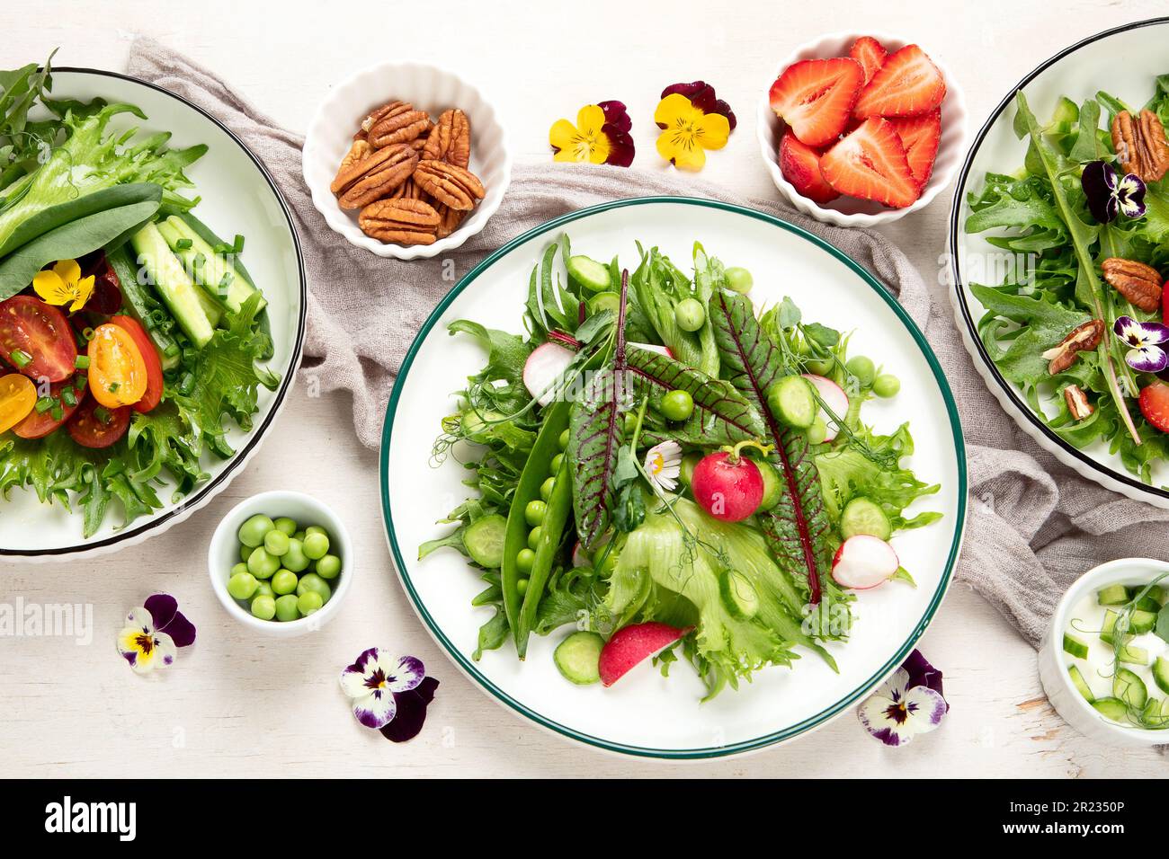 Köstliche Frühlingssalate mit essbaren Blumen, Gemüse, Obst, Mikrogreens und Käse auf weißem Hintergrund. Konzept der sauberen und gesunden Ernährung. Oben vi Stockfoto