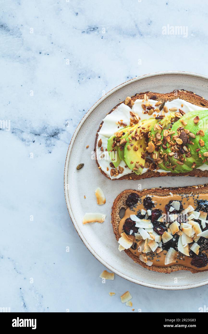 Vegane Frühstückstoasts mit Avocado und Erdnussbutter auf weißem Marmorhintergrund, Blick von oben. Stockfoto