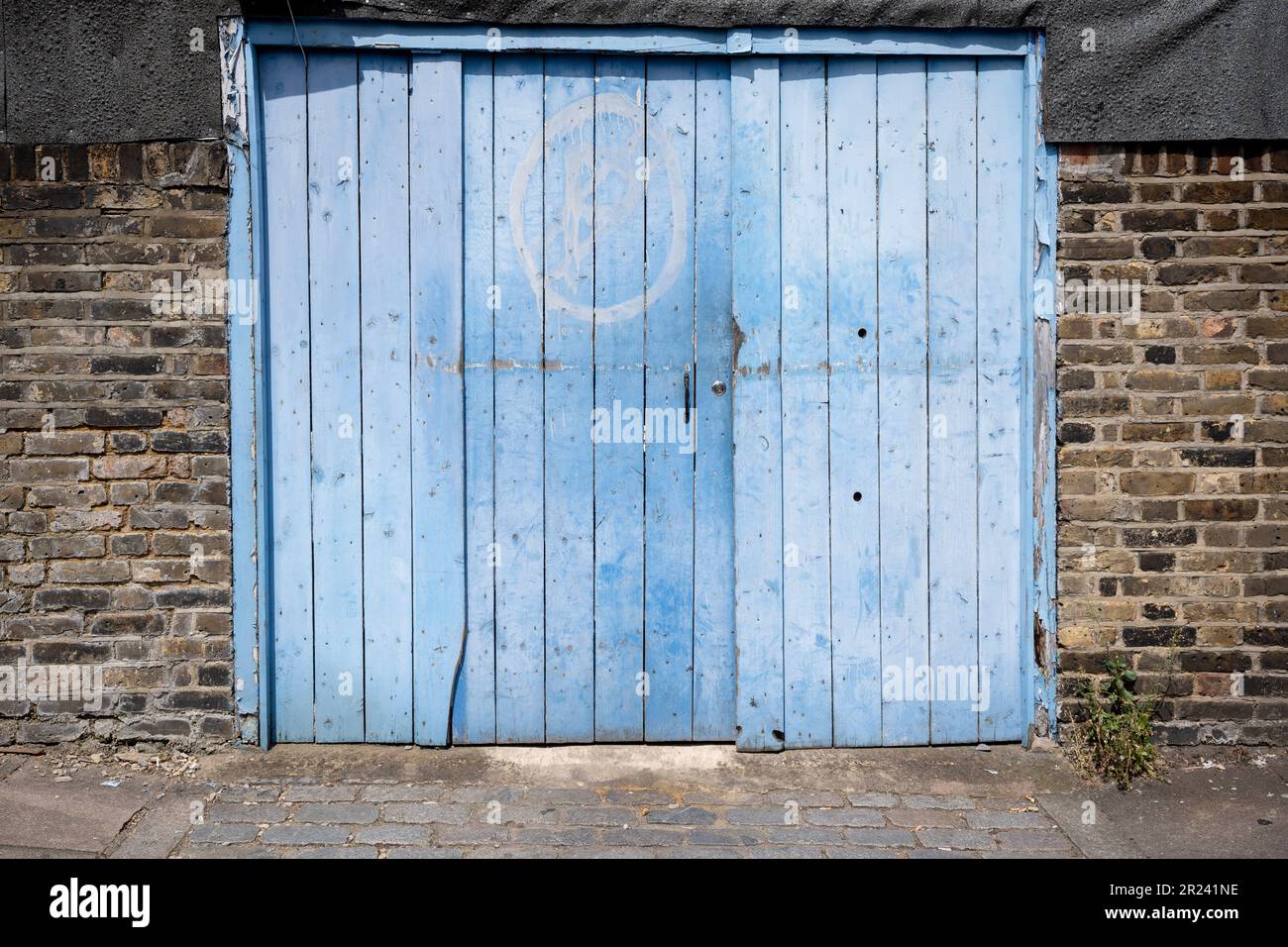 Ein verblichener blauer Garagentor und ein kopfsteingepflasterter Eingang in der Garrett Lane in Earsfield im Süden Londons, am 16. Mai 2023 in London, England. Stockfoto