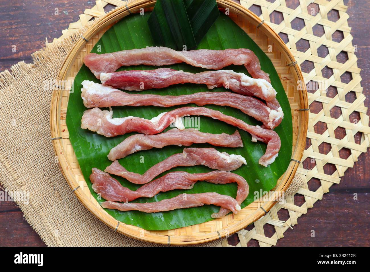 Sonnengetrocknetes Schweinefleisch (nicht gekocht) in Bambusschale aus Holz - thailändisches Essen namens Moo Dad Deaw Stockfoto