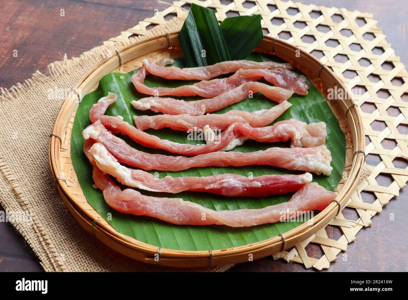 Sonnengetrocknetes Schweinefleisch (nicht gekocht) in Bambusschale aus Holz - thailändisches Essen namens Moo Dad Deaw Stockfoto