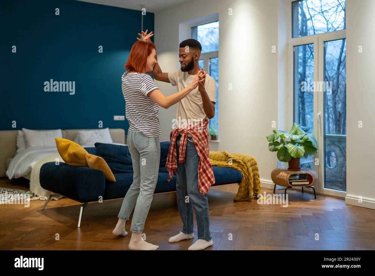 Liebevolles junges, vielfältiges Paar, das romantischen Tanz im modernen Schlafzimmer mit Panoramafenstern tanzt. Stockfoto