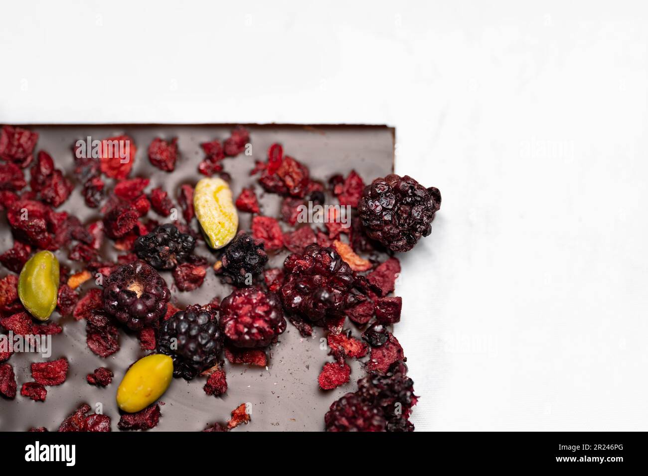 Draufsicht auf ein Schokoladenriegel mit getrockneten Erdbeeren, getrockneten Himbeeren und Pistazien auf weißem Hintergrund. Selektiver Fokus. Stockfoto