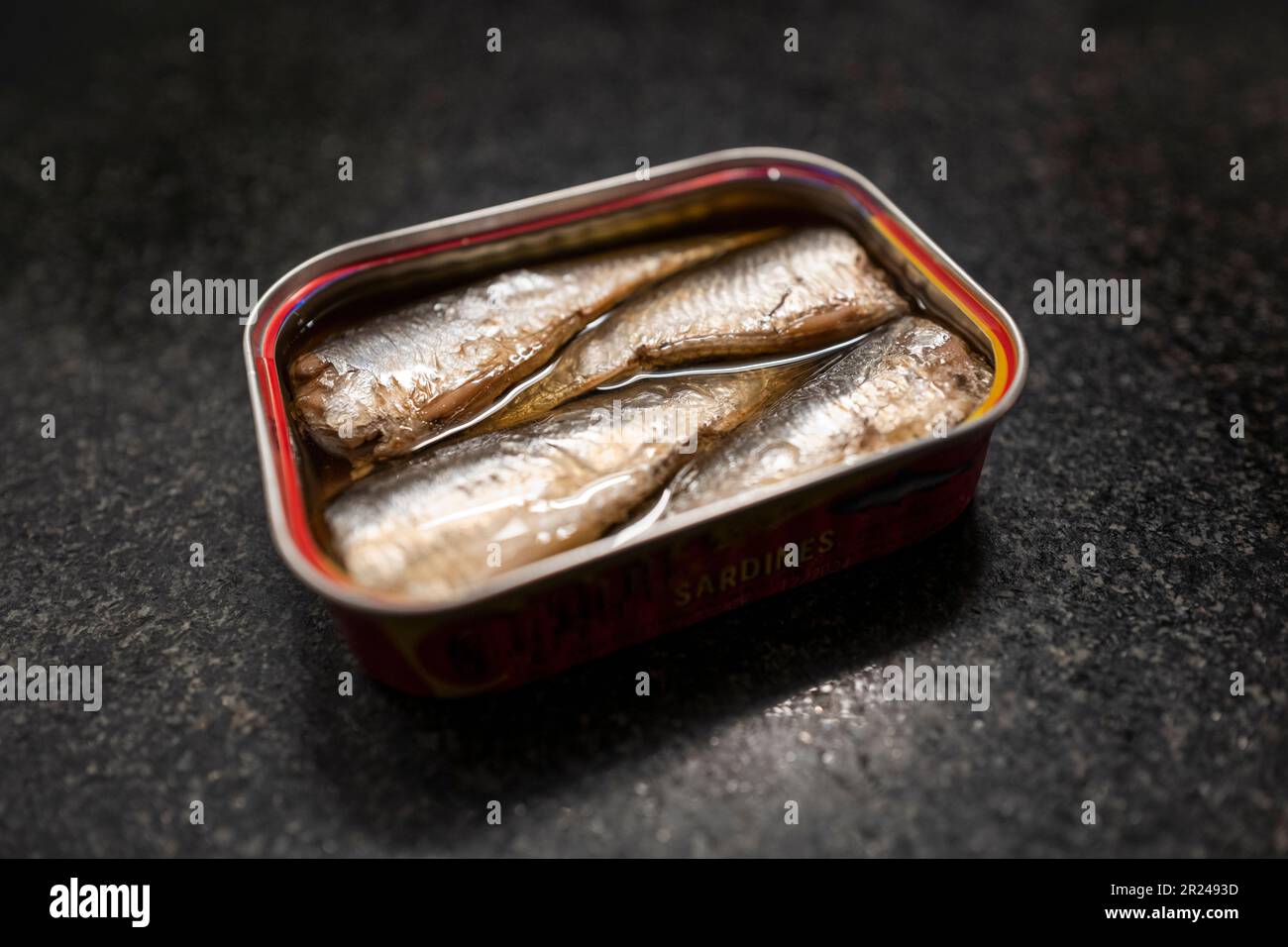 Selektiver Fokus und kreative Hintergrundbeleuchtung auf einer Dose in Sardinen in Öl gegen schwarzen Marmor Stockfoto